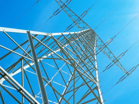 Electricity background banner panorama - Voltage power lines / high voltage electric transmission tower with blue sky and shining sun
